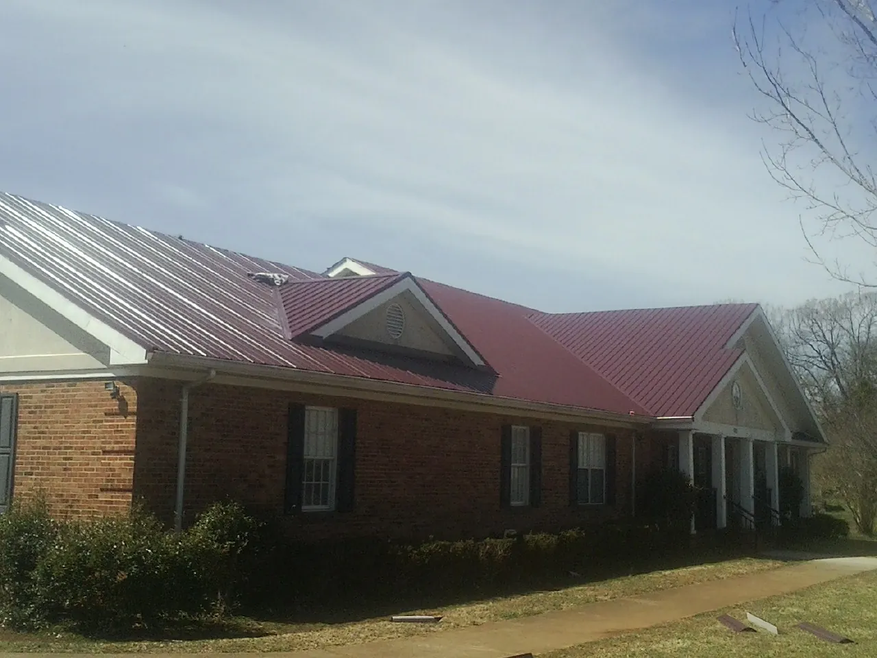 Red metal roof with gabled entries on a long brick building, from a Hail Damage Roof Repair job in Monmouth Beach