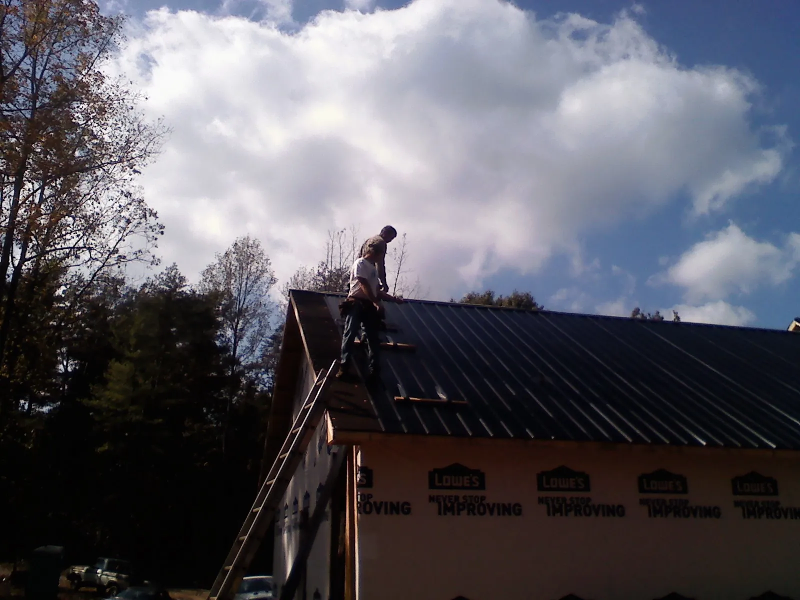 Roofer fastening dark metal panels high against a cloudy sky, from a Roof Inspection job in Monmouth Beach