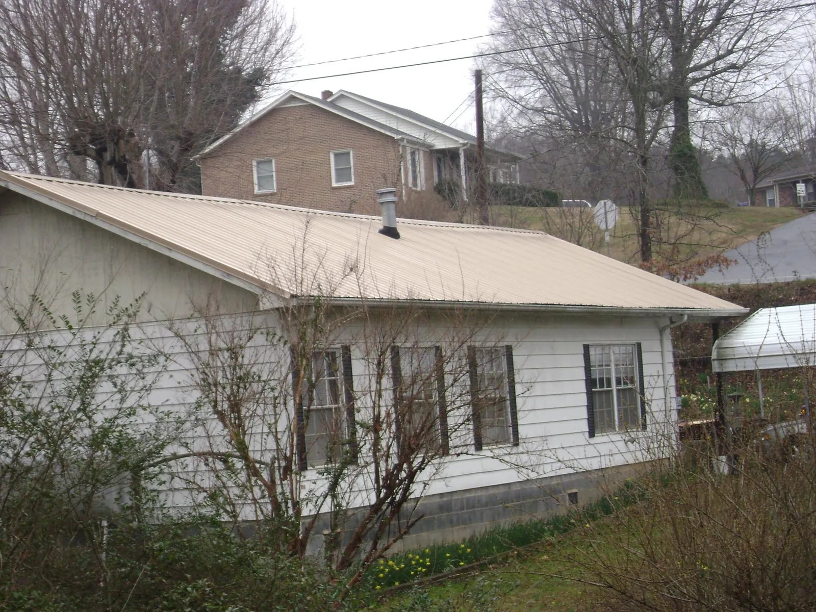 Tan metal roof on a white sided house set into a hillside — Commercial Roofing by Roofing Brothers in Monmouth Beach